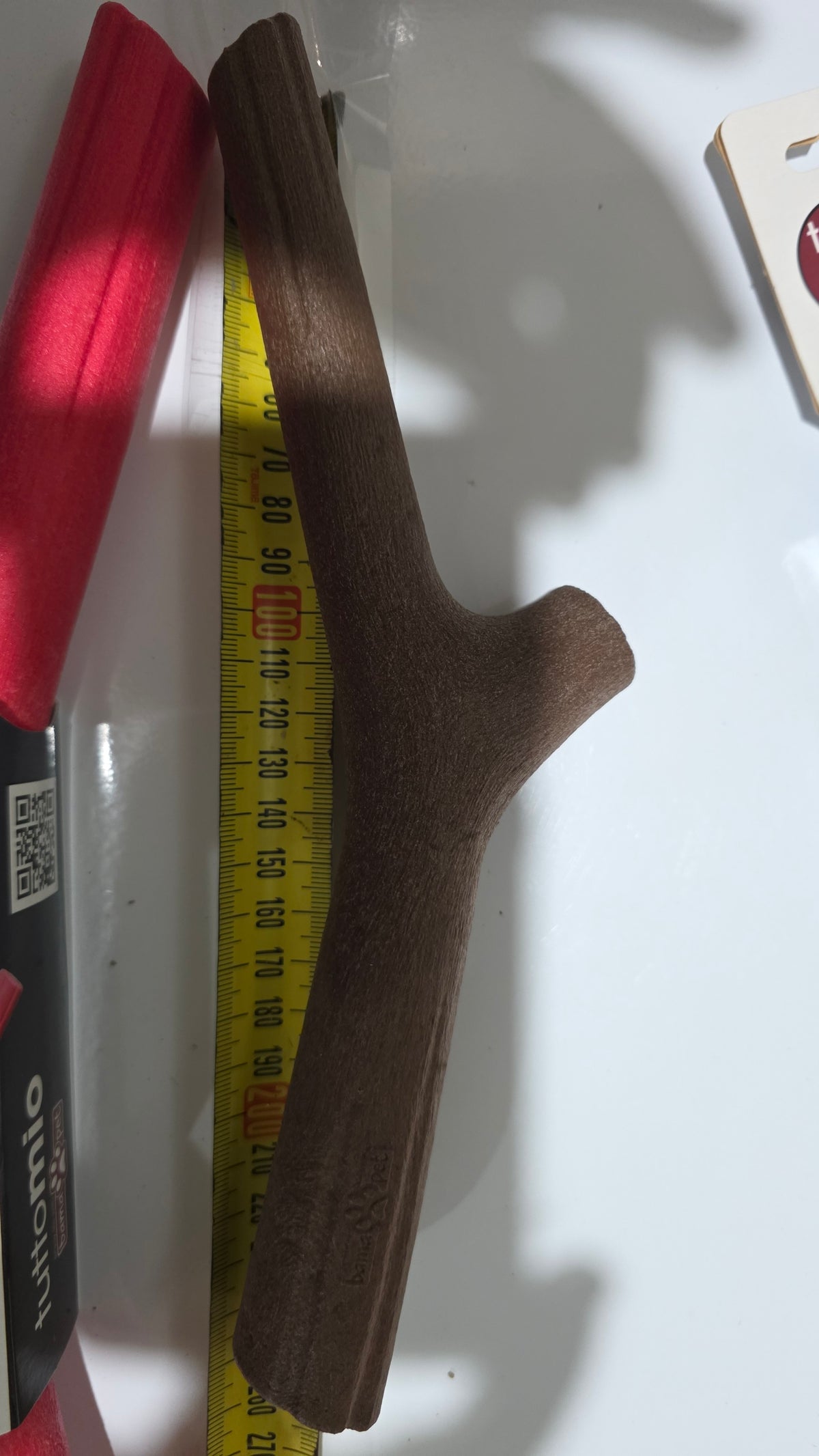 A dark brown dog toy next to a yellow tape measure and a red foam sleeve on a white surface.